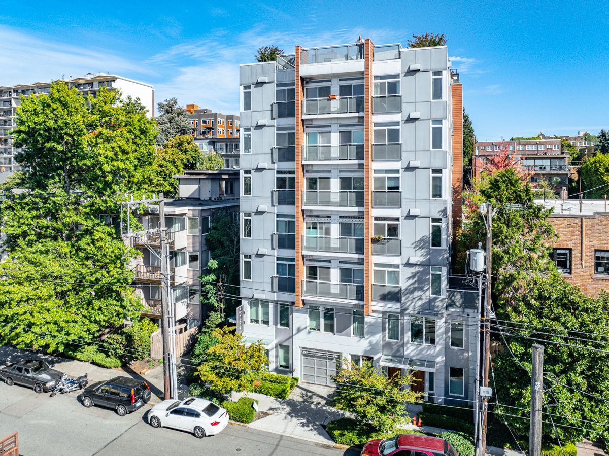 Modern apartment building with balconies and trees on a sunny city street