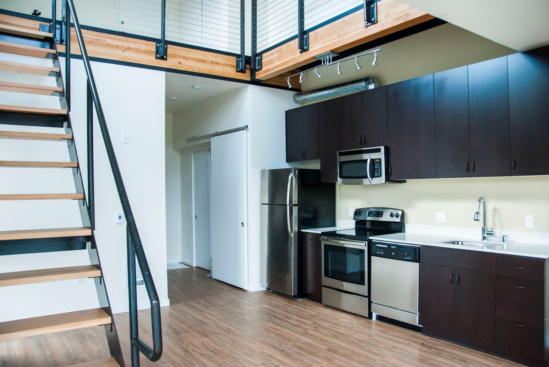Open loft kitchen with dark cabinets, stainless appliances, and a staircase to the upper level