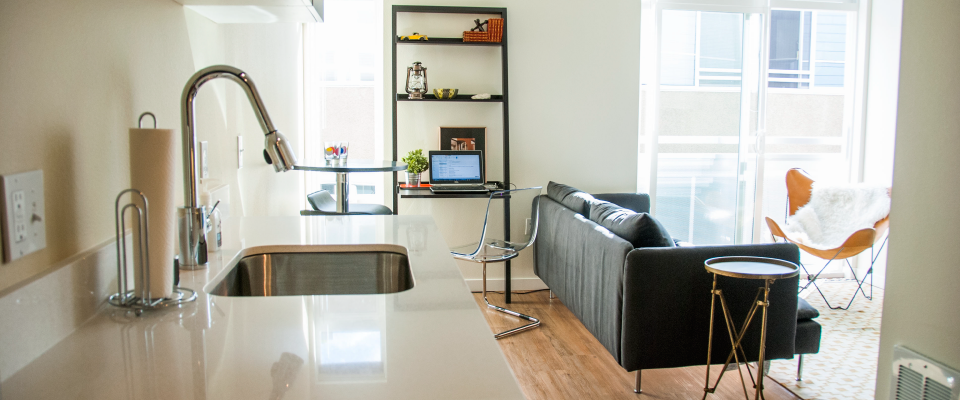 Bright open kitchen and living room with a black sofa, white chairs, and modern decor