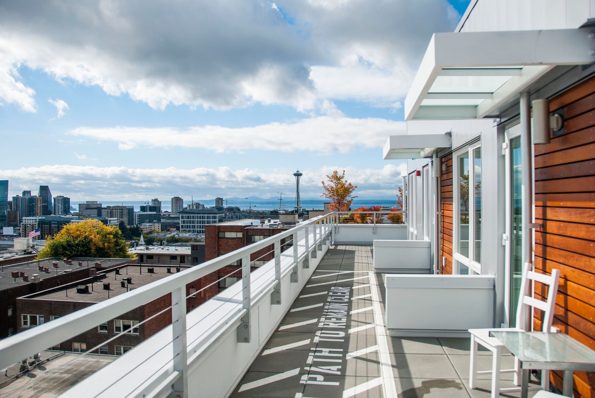 Rooftop terrace with white railing, lounge chairs, city skyline, and cloudy sky