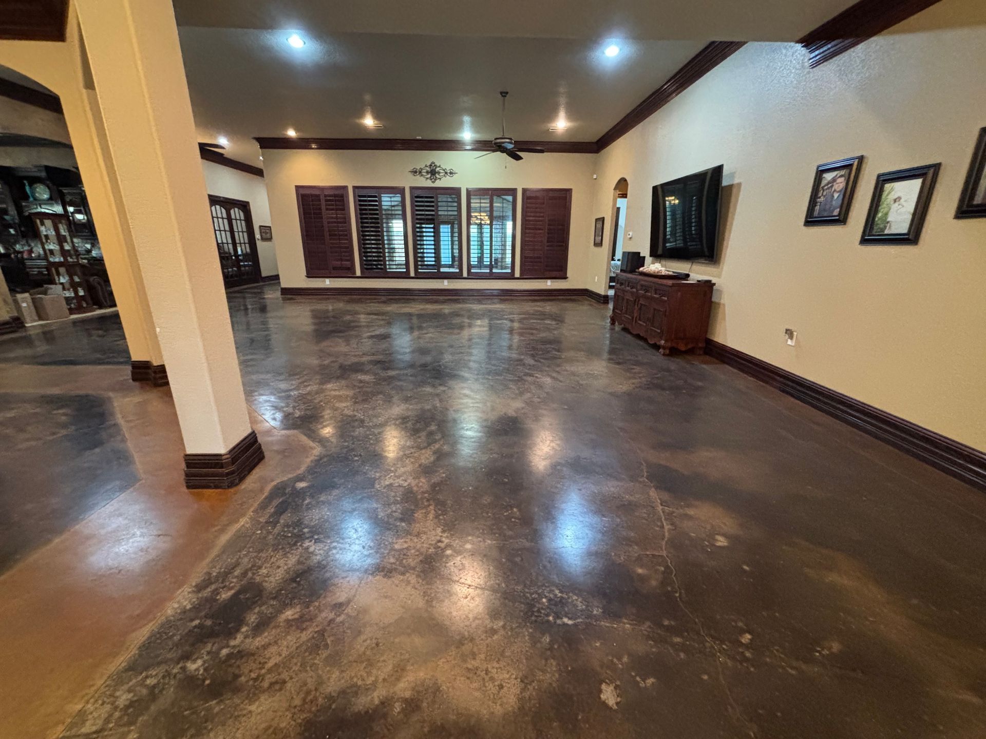 Spacious room with stained concrete floor, dark wood trim, and windows with decorative shutters.