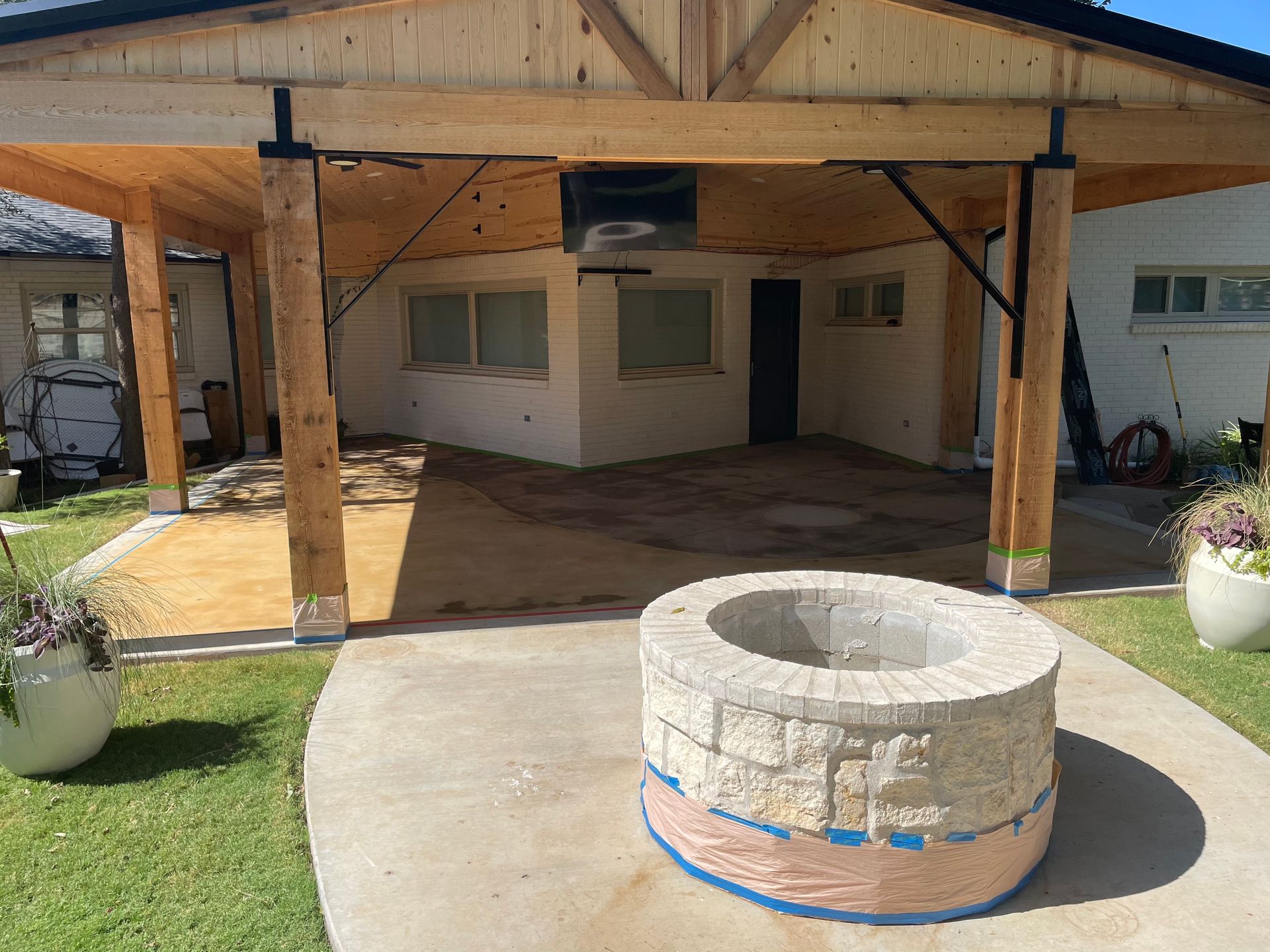 Outdoor patio with wooden beams, concrete fire pit, and a small building.