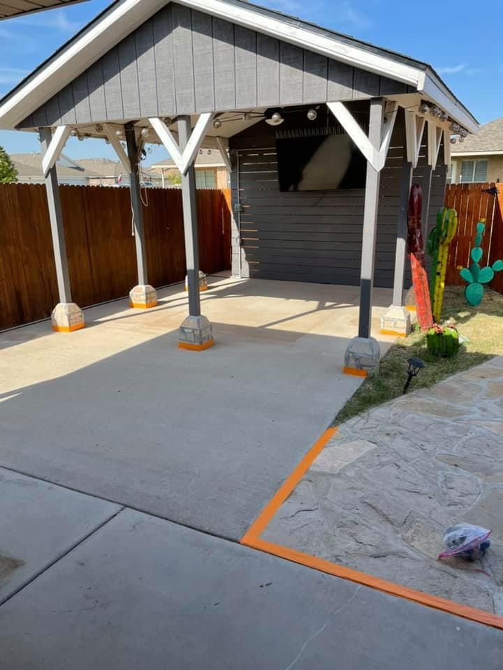 Concrete patio with a dark grey shed/carport, wooden fence, and outdoor decor.