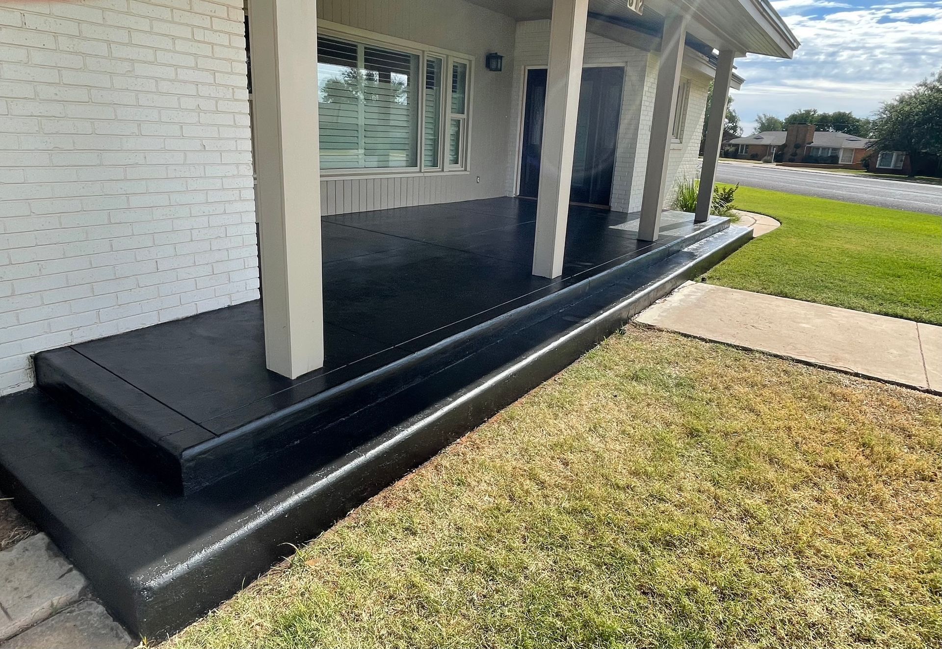 Black painted concrete porch with columns, a step, and green lawn.