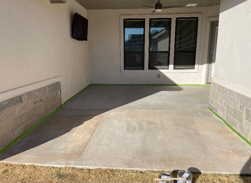 Concrete patio with green tape along edges, preparing for painting near a window.