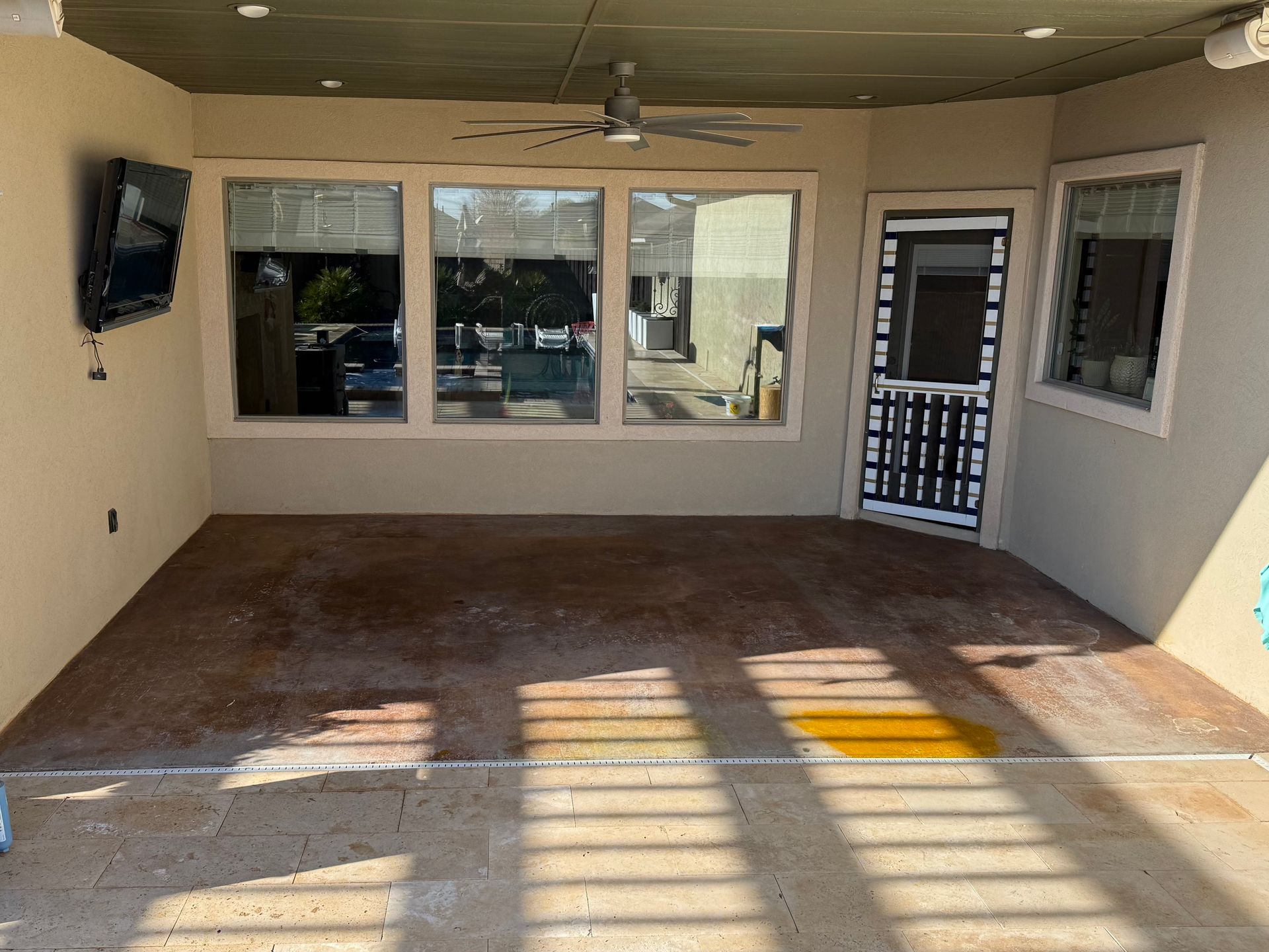 Covered patio with windows, door, TV, ceiling fan, and stained floor.