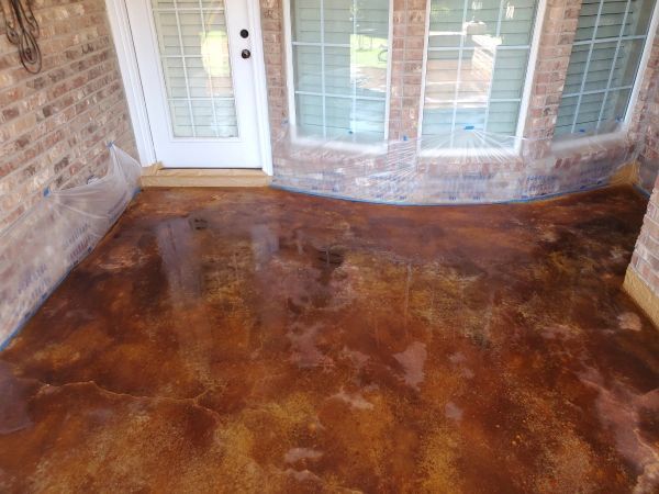 Brown and gold stained concrete patio with brick wall and glass windows. White door visible.