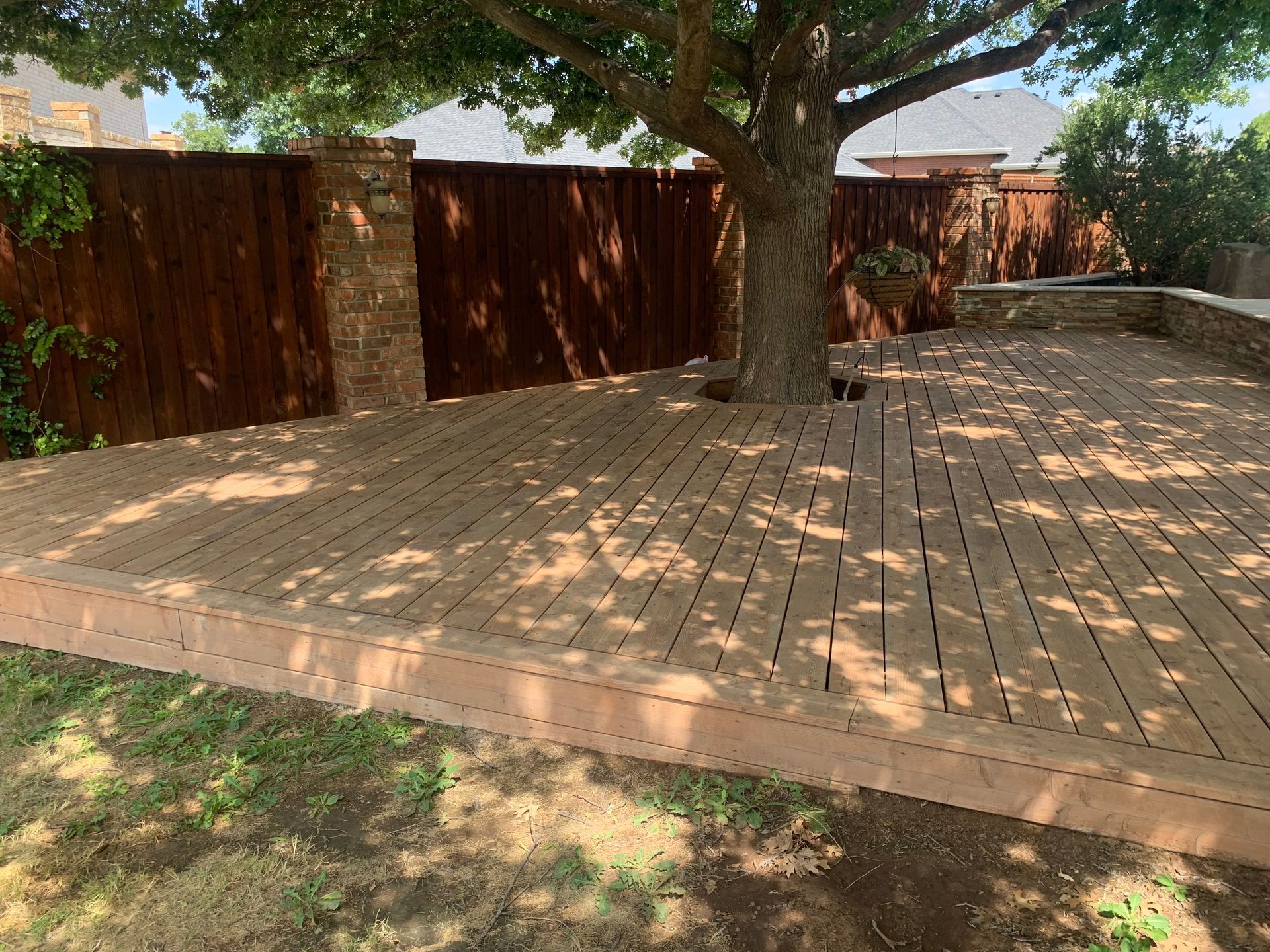 Wooden deck surrounding a tree in a backyard, with a brown fence in the background.