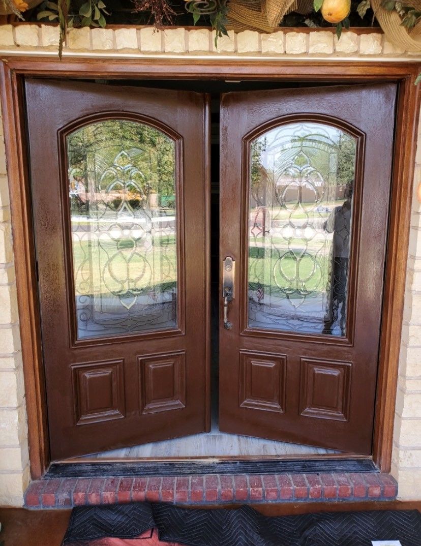 Brown double front doors with arched glass panels and decorative inlays, framed by brick and stone.