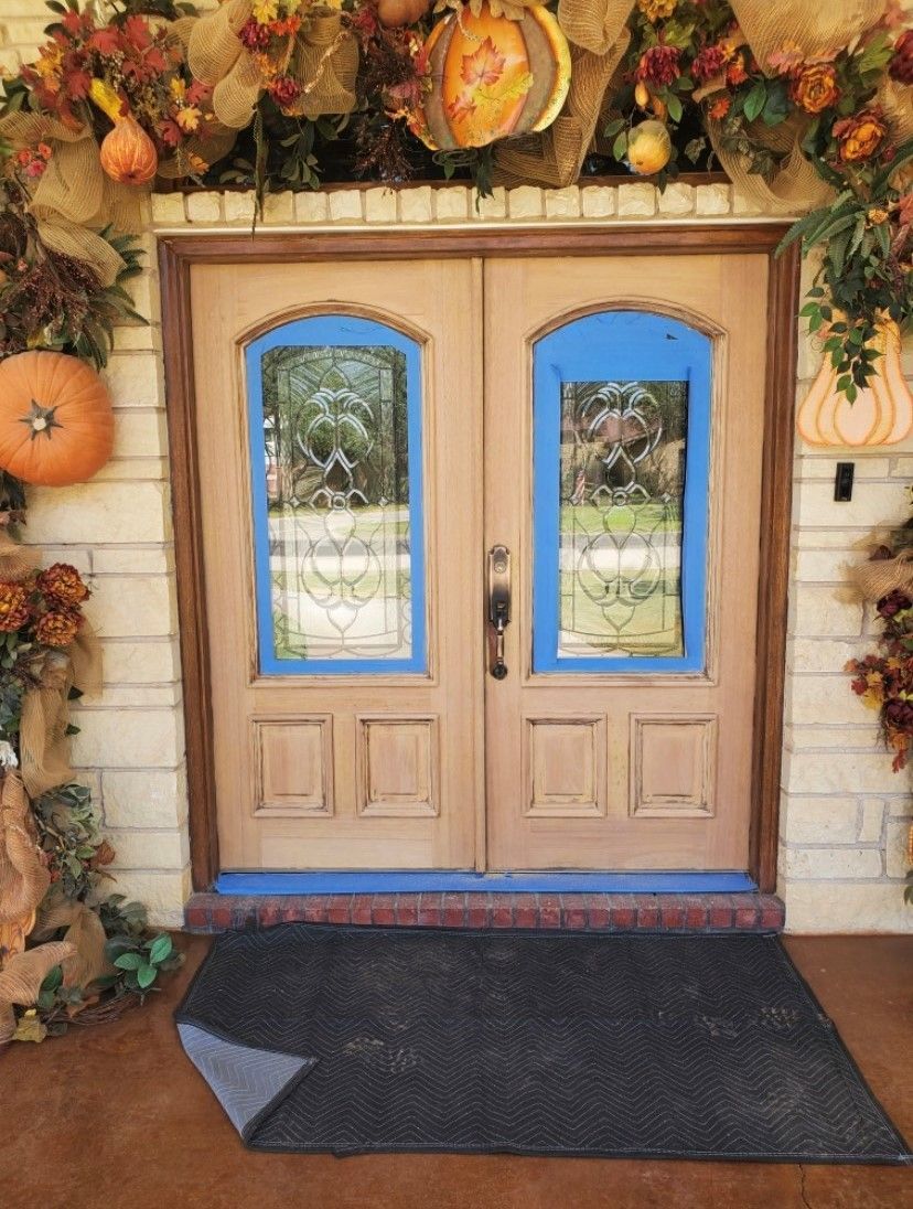 Double wooden doors with blue trim, decorated with fall foliage and pumpkins.