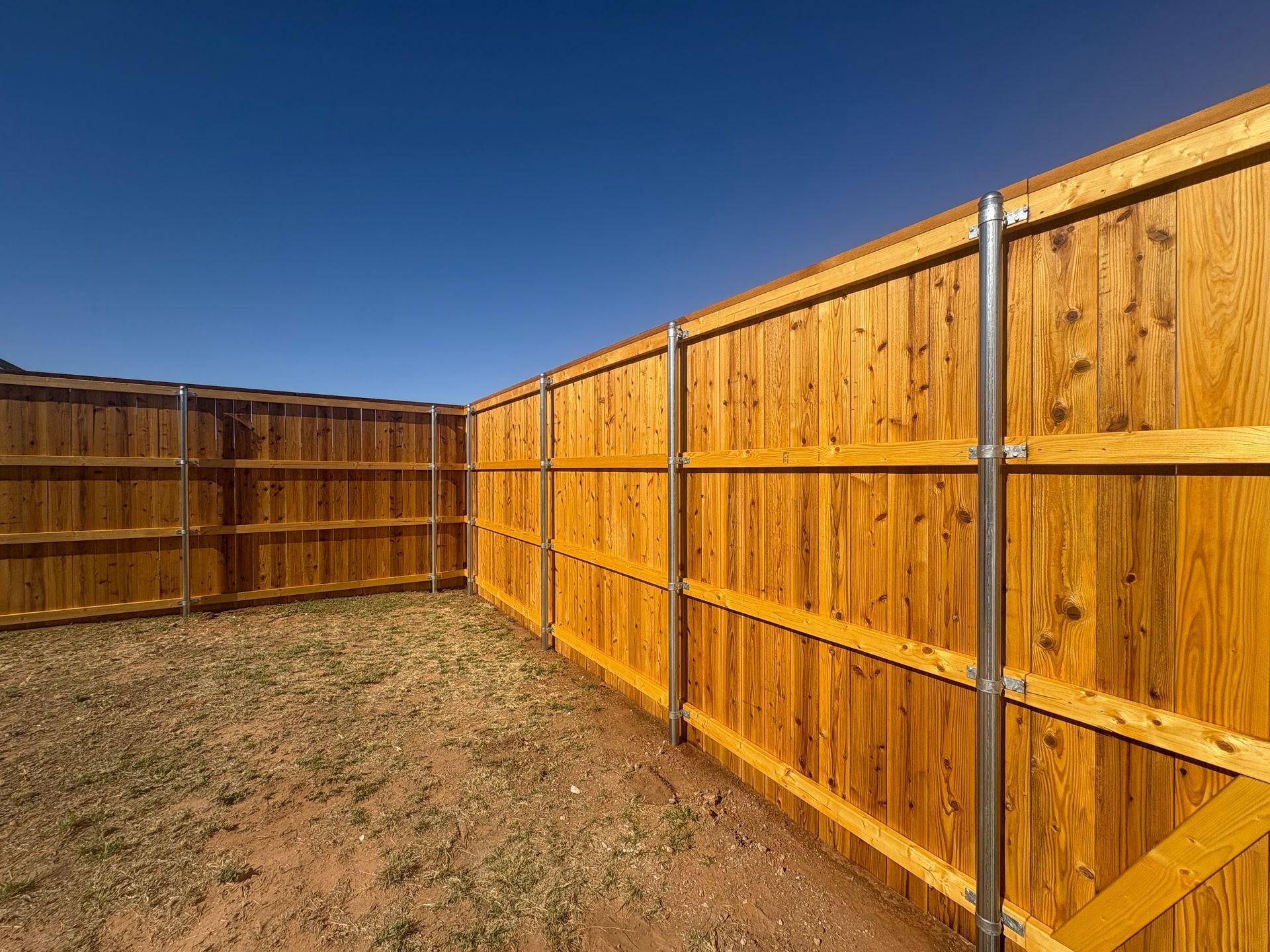 Wooden fence surrounding a yard against a clear blue sky.