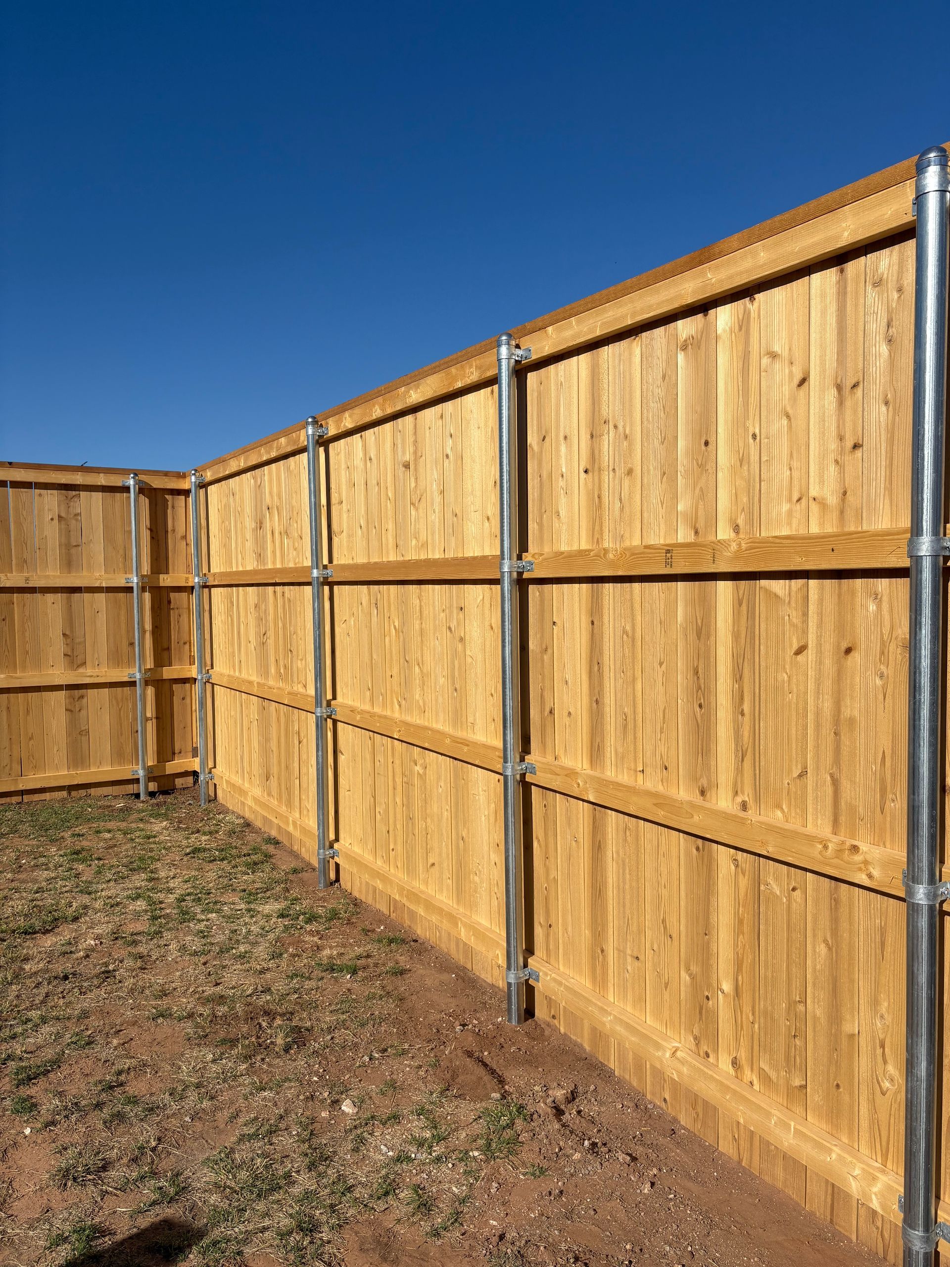 Wooden fence with metal posts against a blue sky, on dry ground.