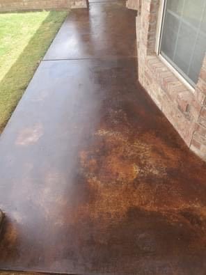 Brown stained concrete porch with variations in color. Next to green grass and a brick wall.