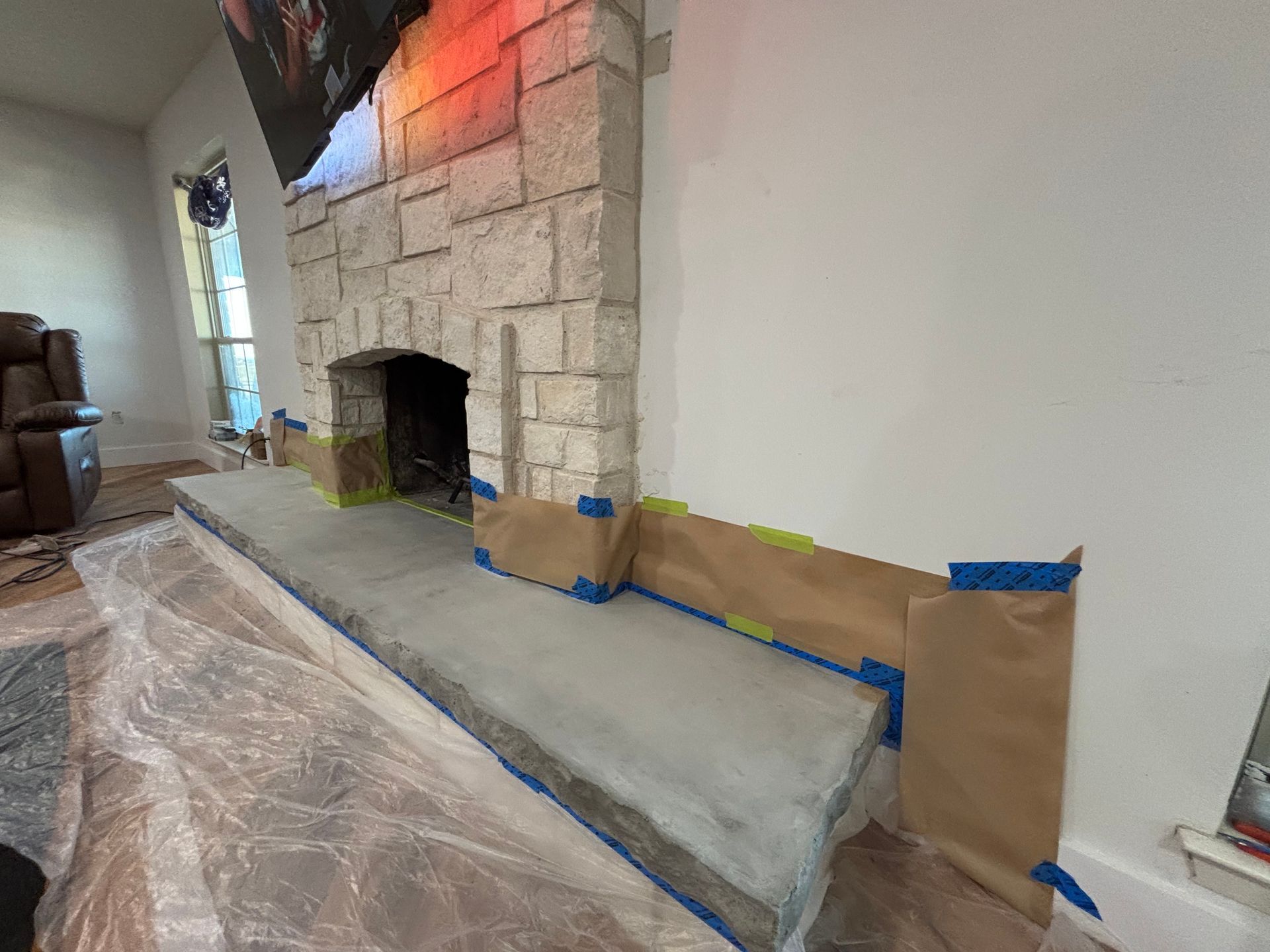 Fireplace with stone surround, concrete hearth under construction, masked with paper and tape.