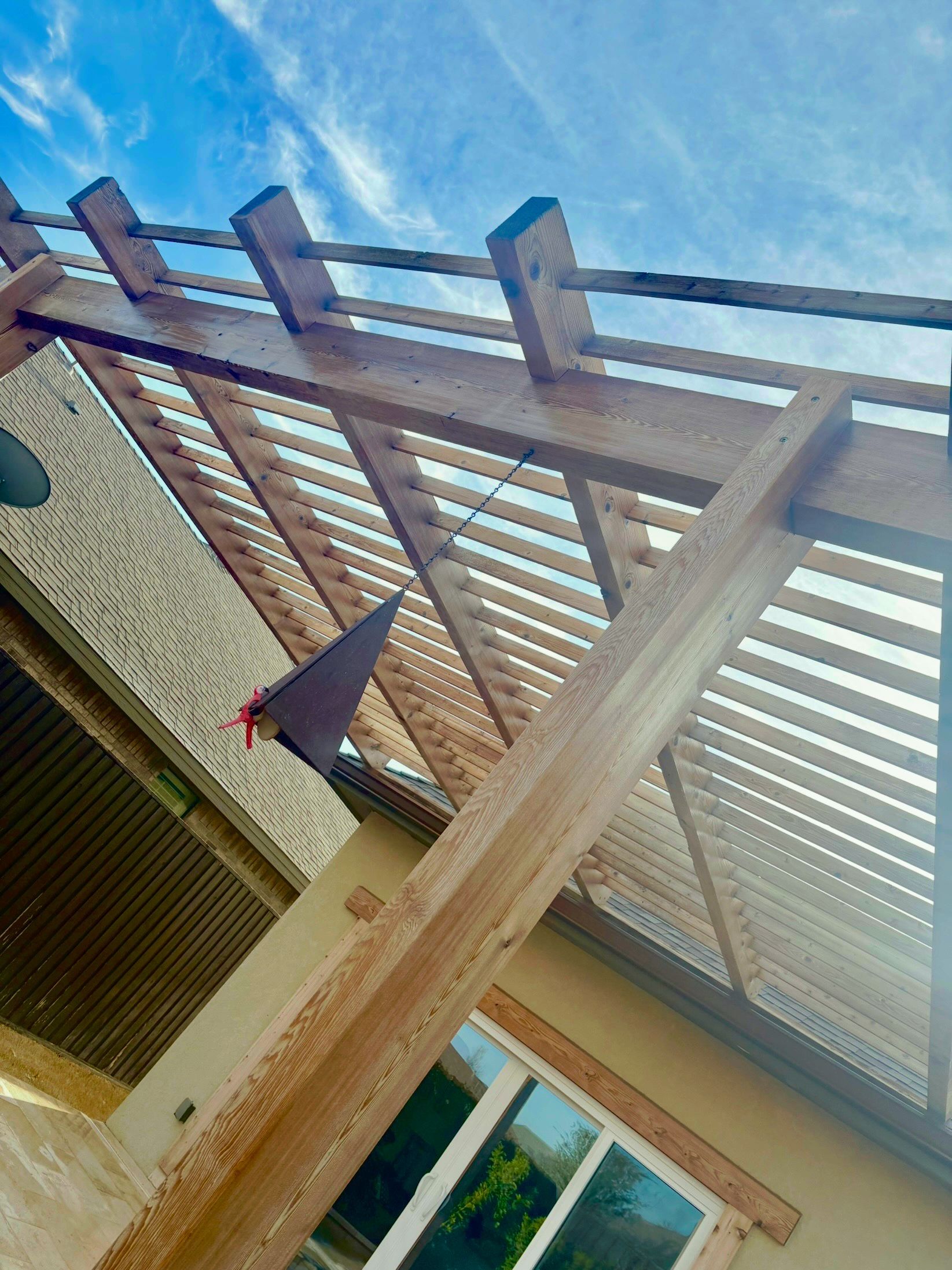 Wooden pergola casting shadows; blue sky visible through slats. Window below.