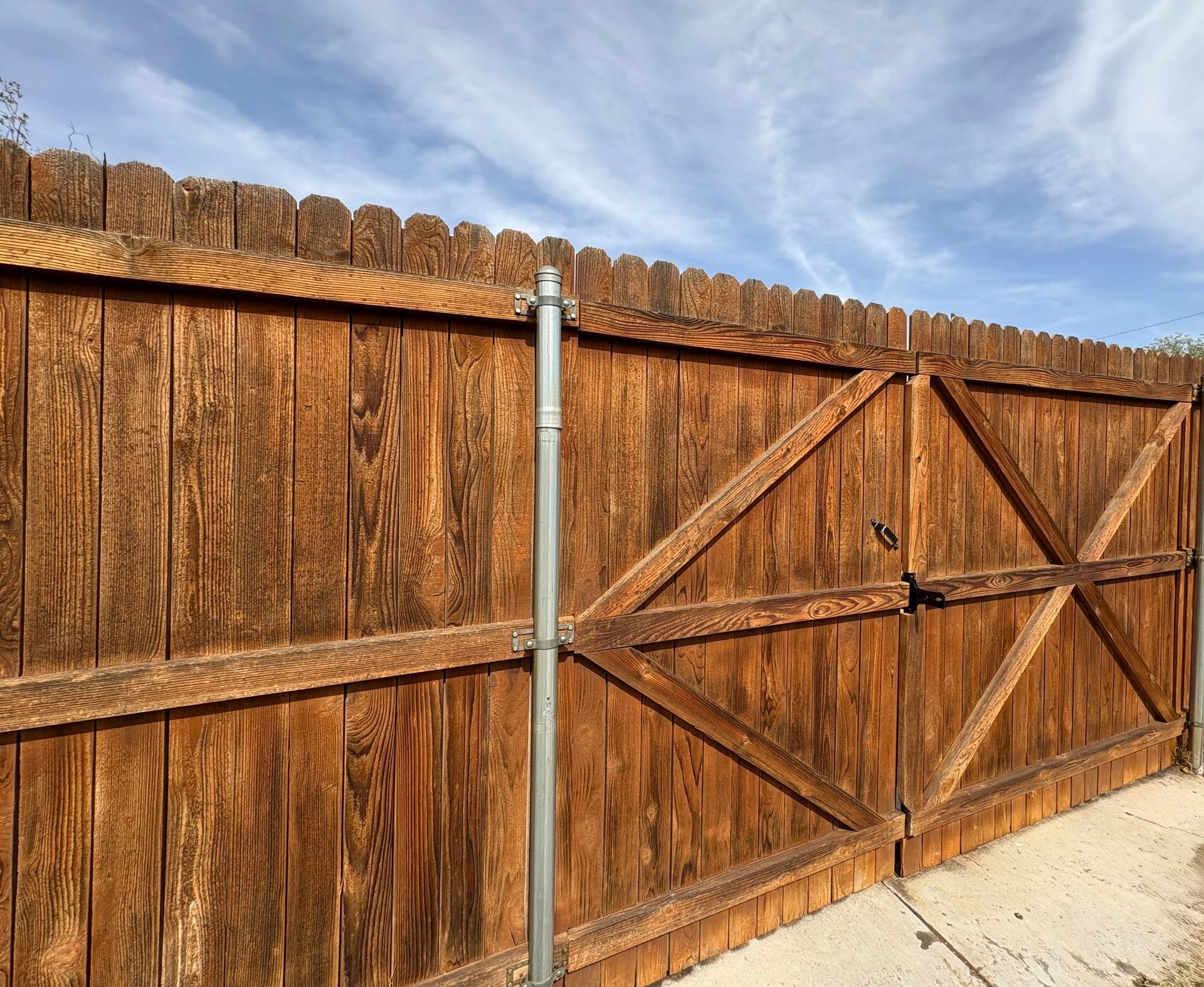 Wooden fence and gate with metal post against a partly cloudy sky.