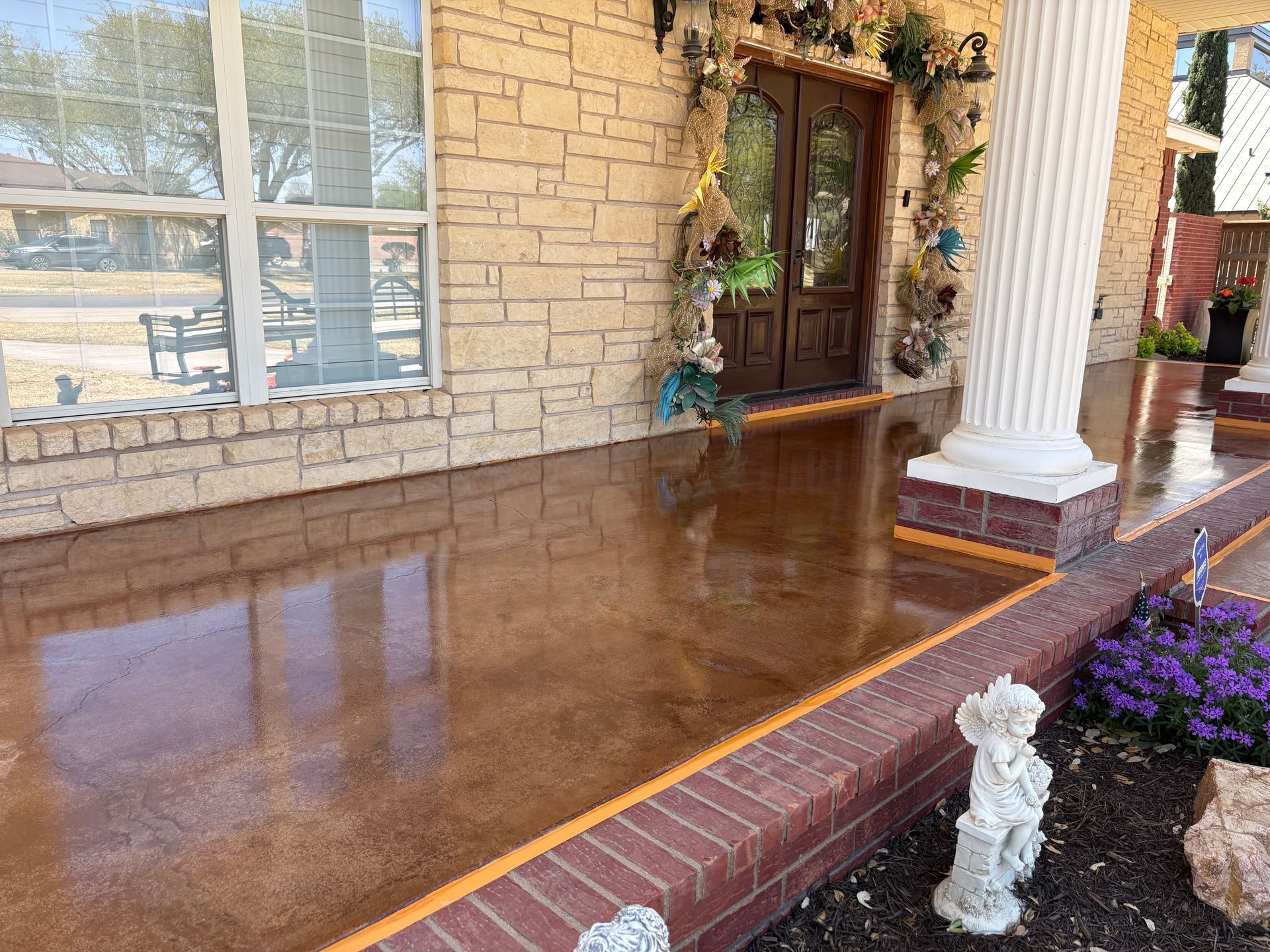 Brown concrete porch with brick trim, a white pillar, and a front door with decorations.