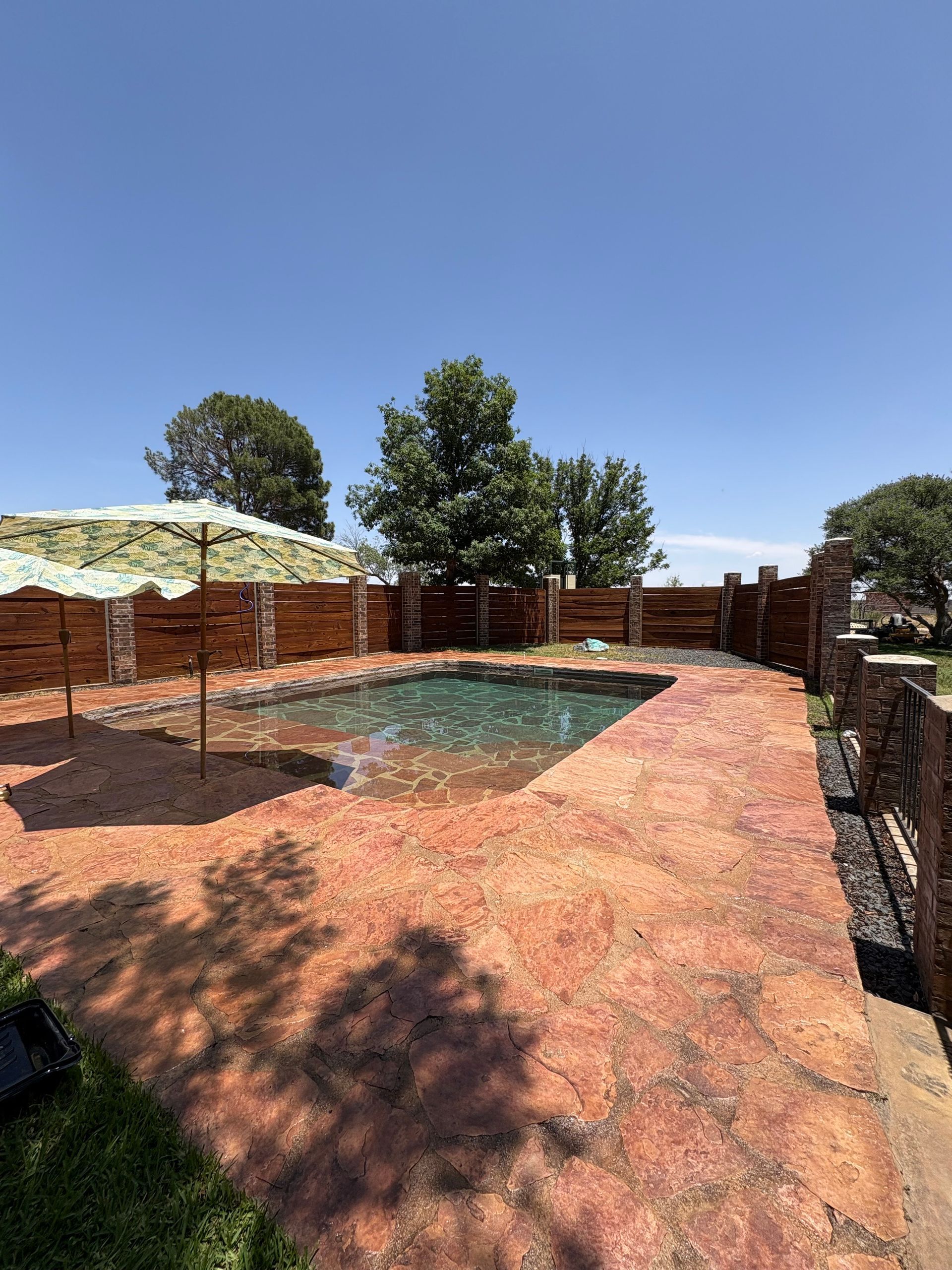 Backyard with a pool, stained concrete patio, and wooden fence on a sunny day.