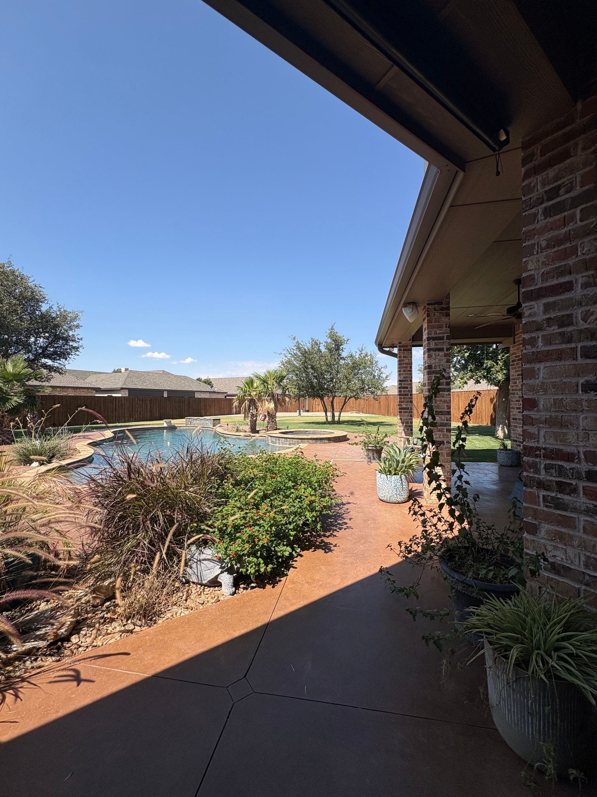 Backyard with pool, patio, and brick house under a blue sky.