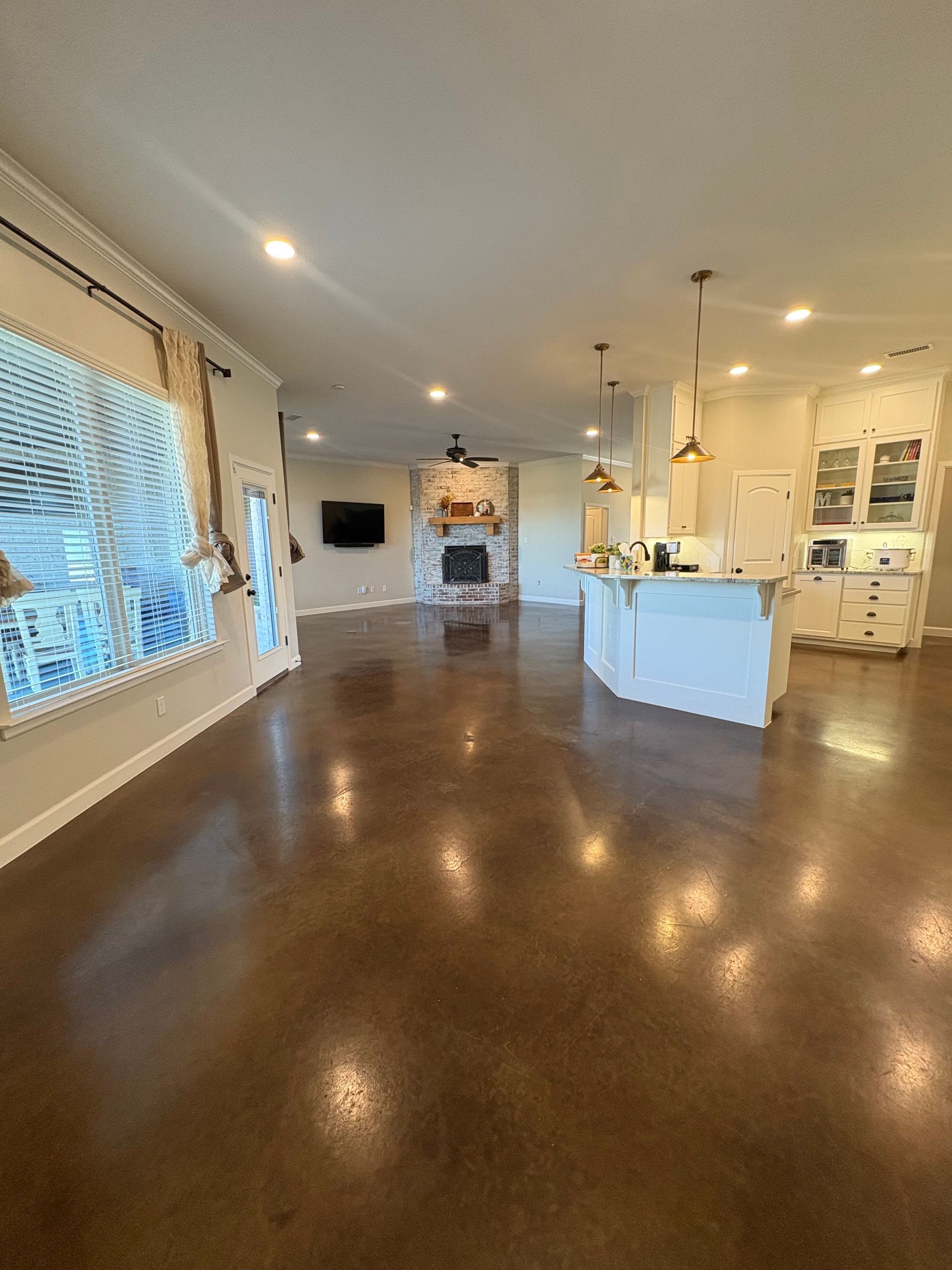 Open-plan interior with brown polished concrete floor, kitchen island, fireplace, and large windows.