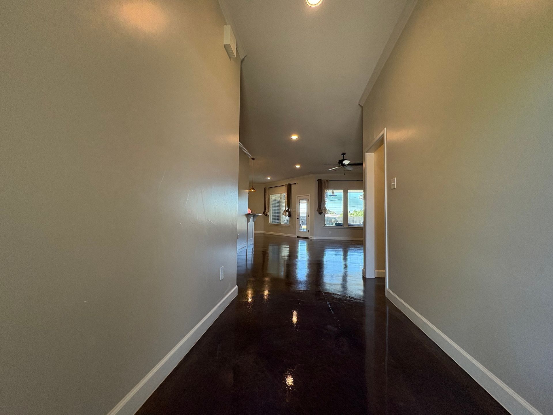 Long hallway with dark shiny floor, beige walls, and doorways leading to other rooms.