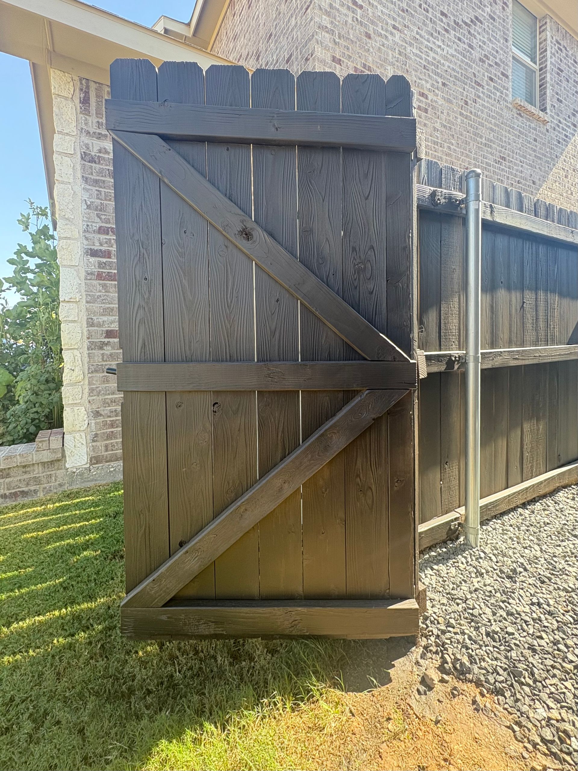 Wooden gate in front of a fence, painted dark brown, with a diagonal brace.