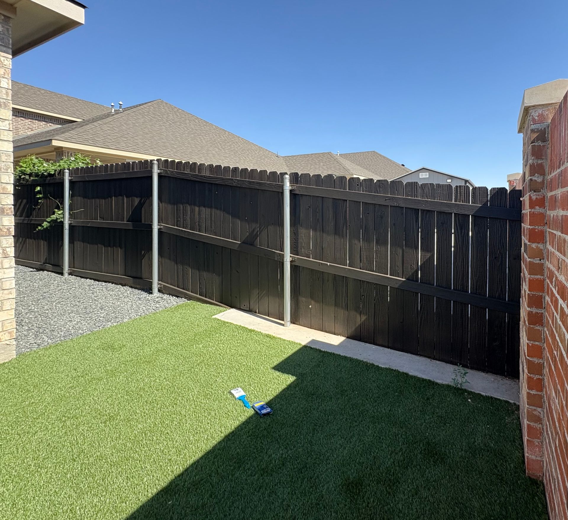A backyard with artificial turf, a black wooden fence, and a brick wall.