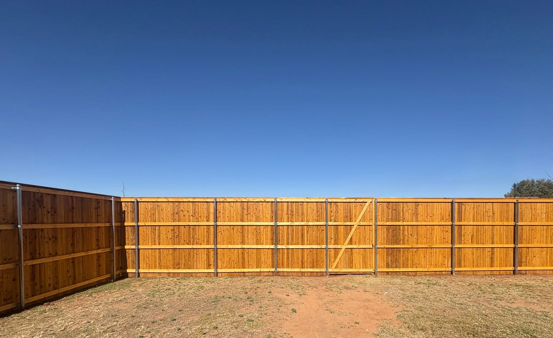 Wooden fence against a clear blue sky in a yard.