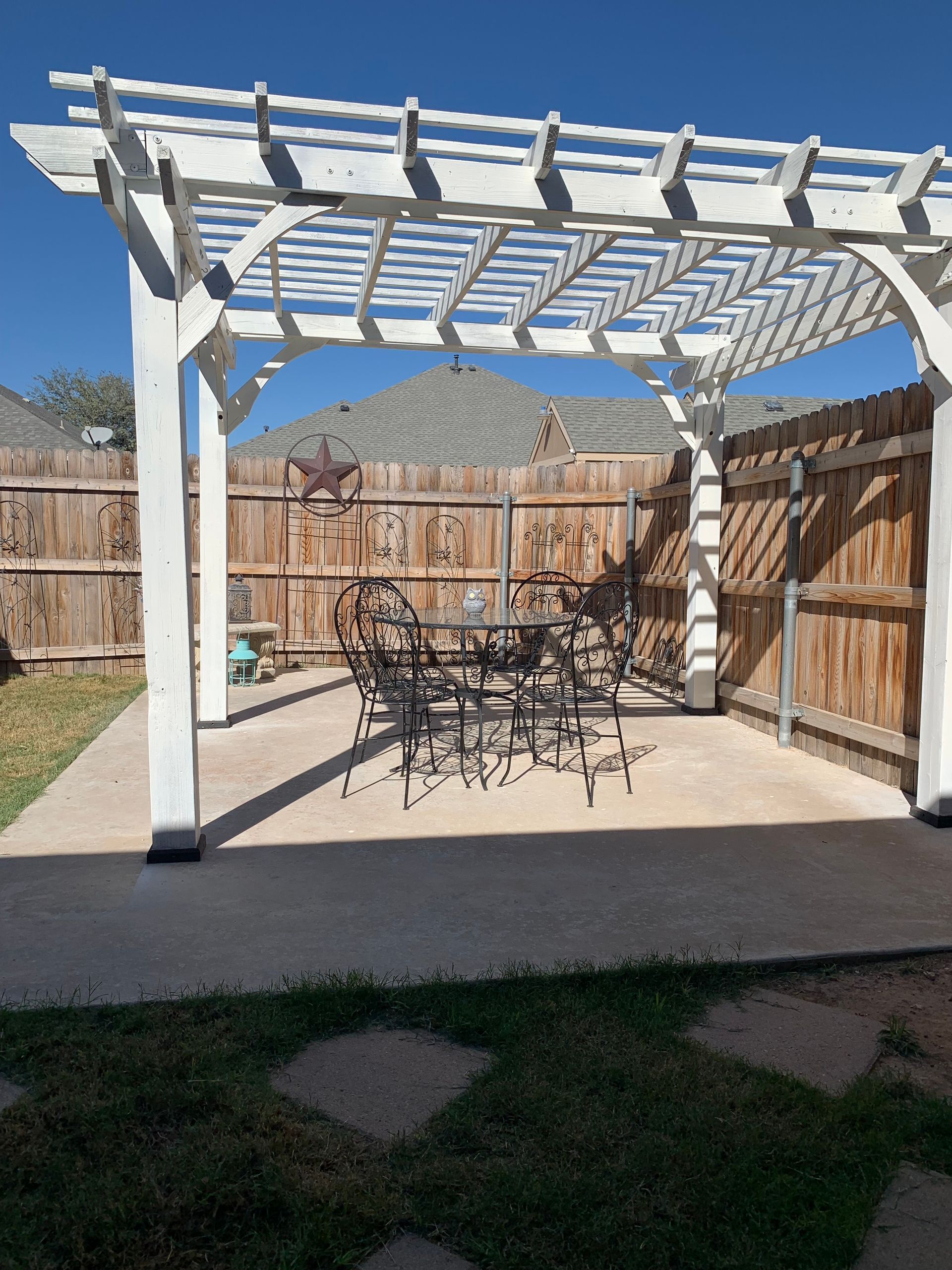 White pergola over patio with table and chairs, brown fence, and mountain in the background.