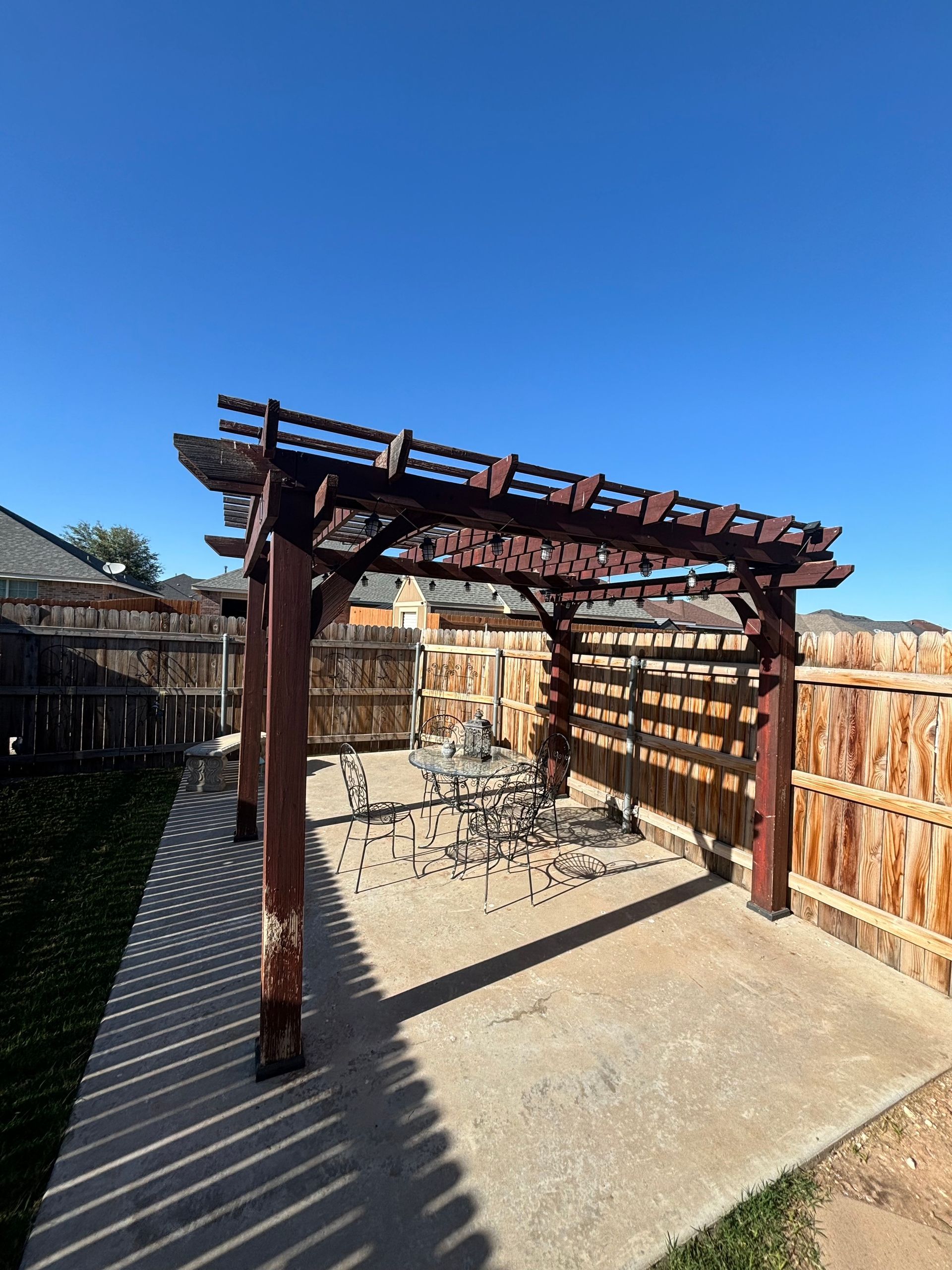 Wooden pergola over a concrete patio in a backyard; sunny day.