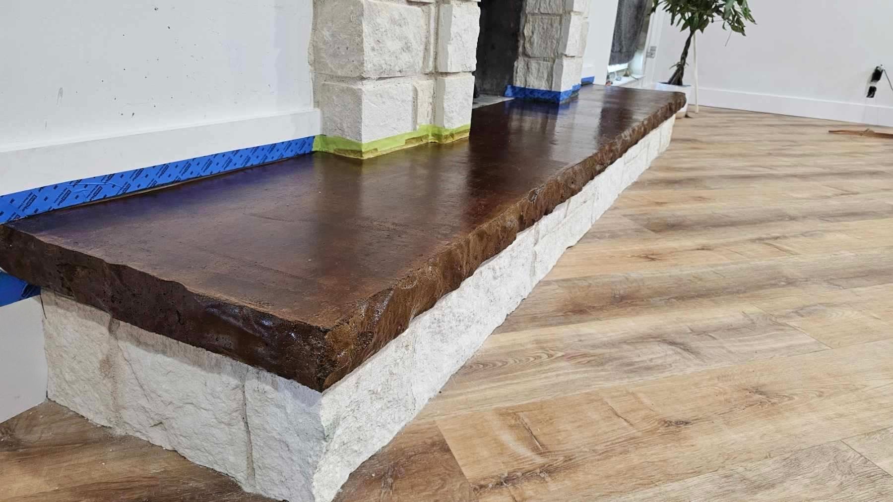 Stone shelf with brown top, white stone base, and blue painter's tape; near wood-look flooring.