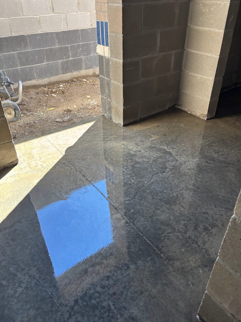A glossy, dark gray concrete floor reflecting the blue sky, situated near unfinished masonry block walls.