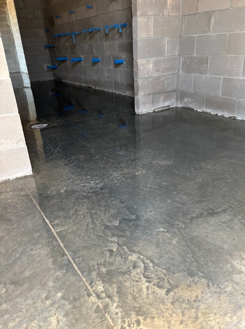 Concrete room with standing water on the floor and blue plastic pipes mounted on the block walls.