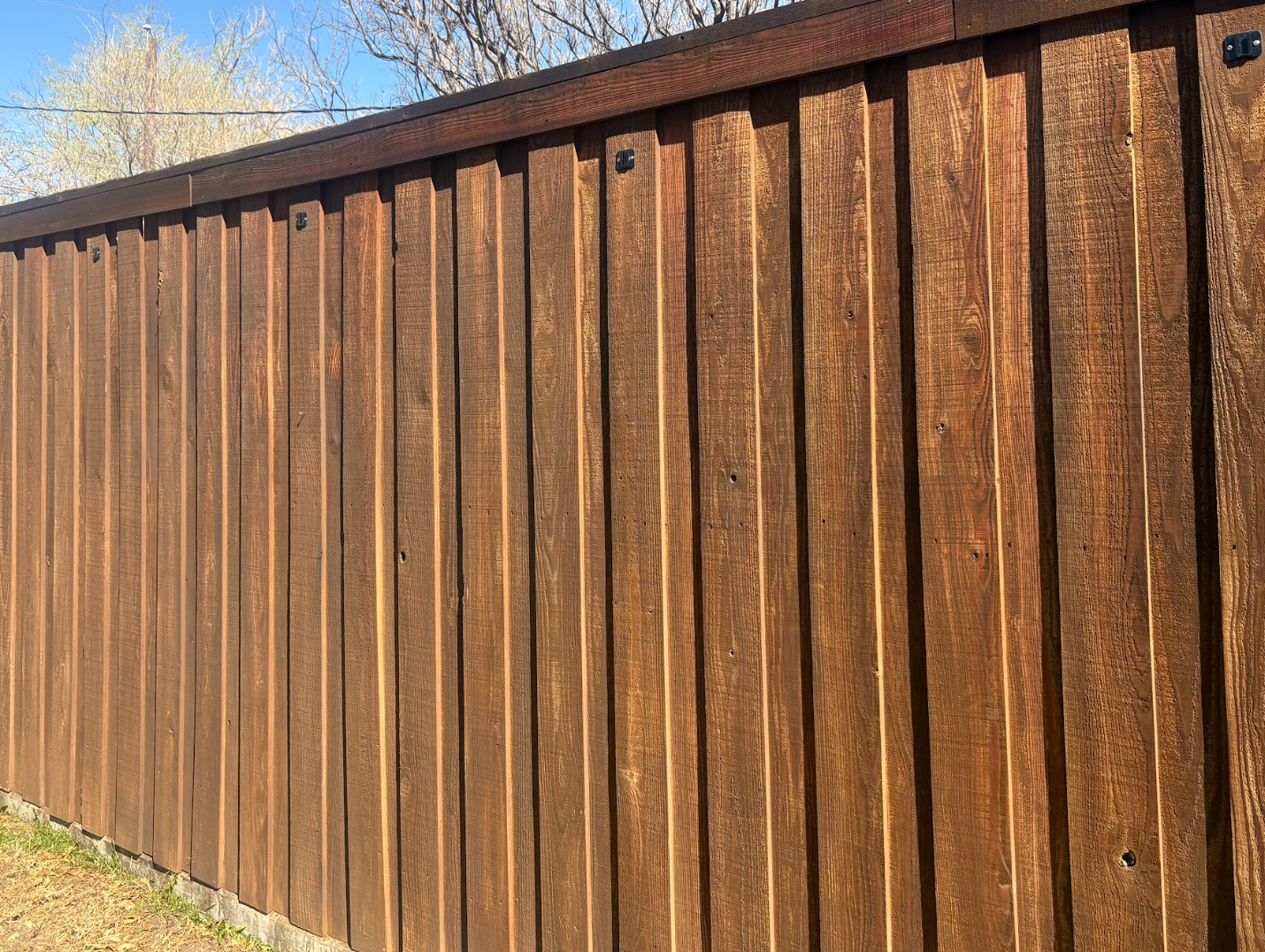 A wooden fence with vertical boards in a warm brown tone, viewed from a slight angle under a blue sky.
