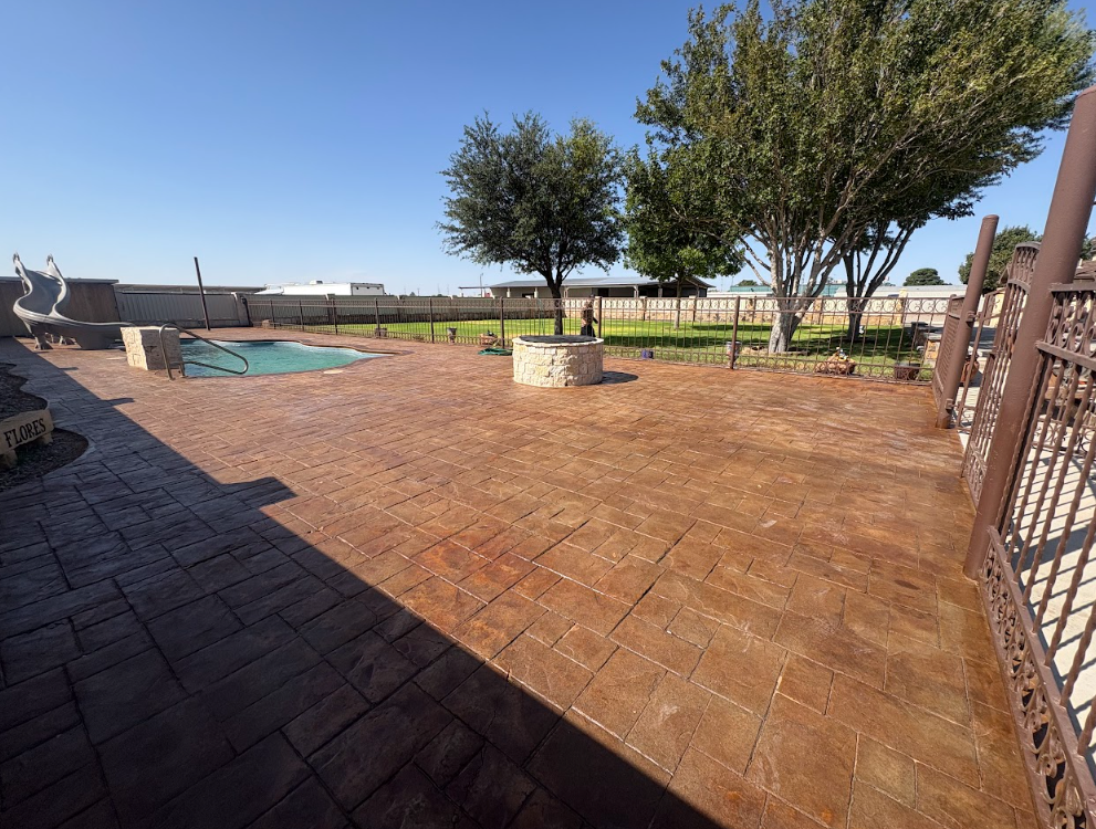Spacious backyard patio with reddish tile, a small pool, trees, and fenced open field beyond.