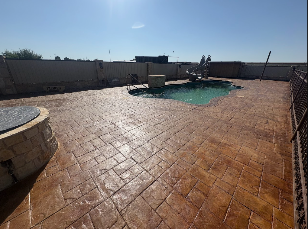 Empty backyard patio with stamped concrete and a swimming pool under a bright blue sky