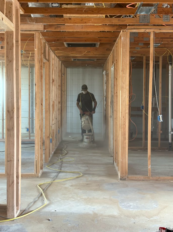 Partially built interior hallway with exposed wood framing and a worker walking away in the distance