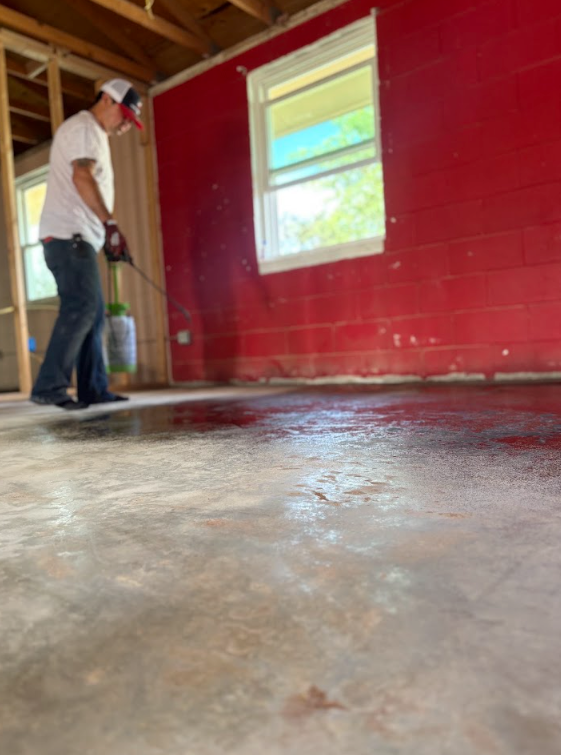 Person painting a red interior wall near a window in an unfinished room