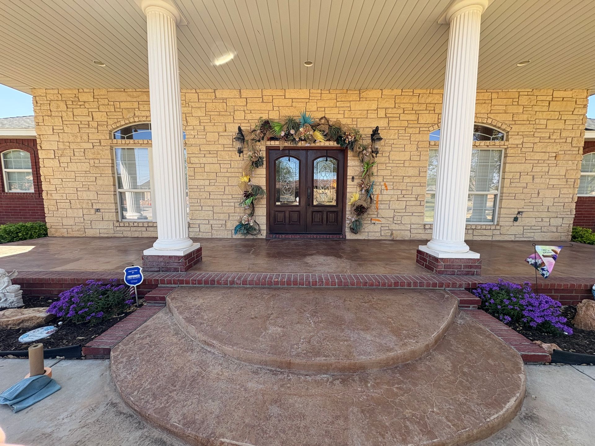 Stone home exterior with covered porch, ornate columns, double doors, and decorative archway.