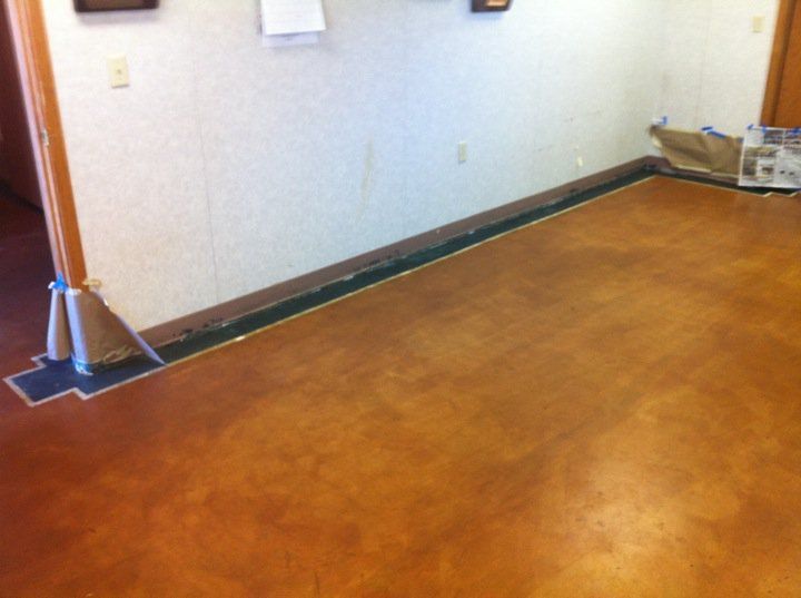Brown and gold stained concrete floor with dark border against a white wall and a support beam.