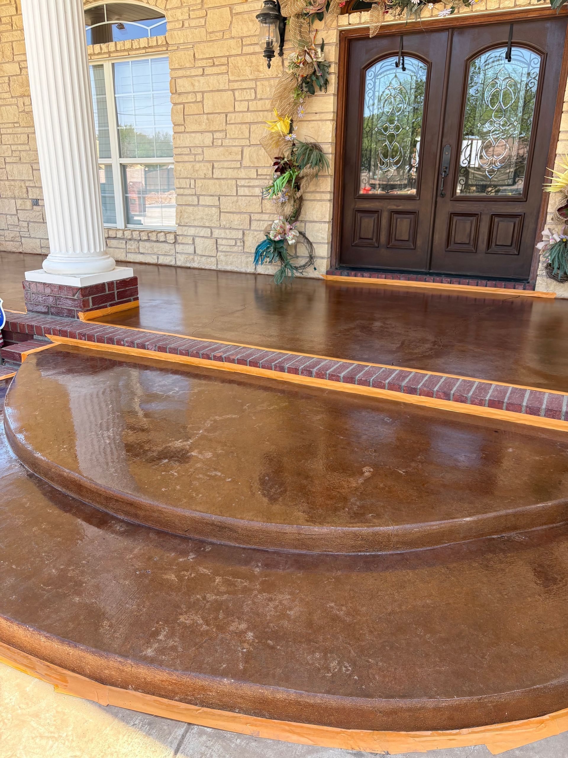 Brown stained concrete porch with steps leading to double doors of a house.