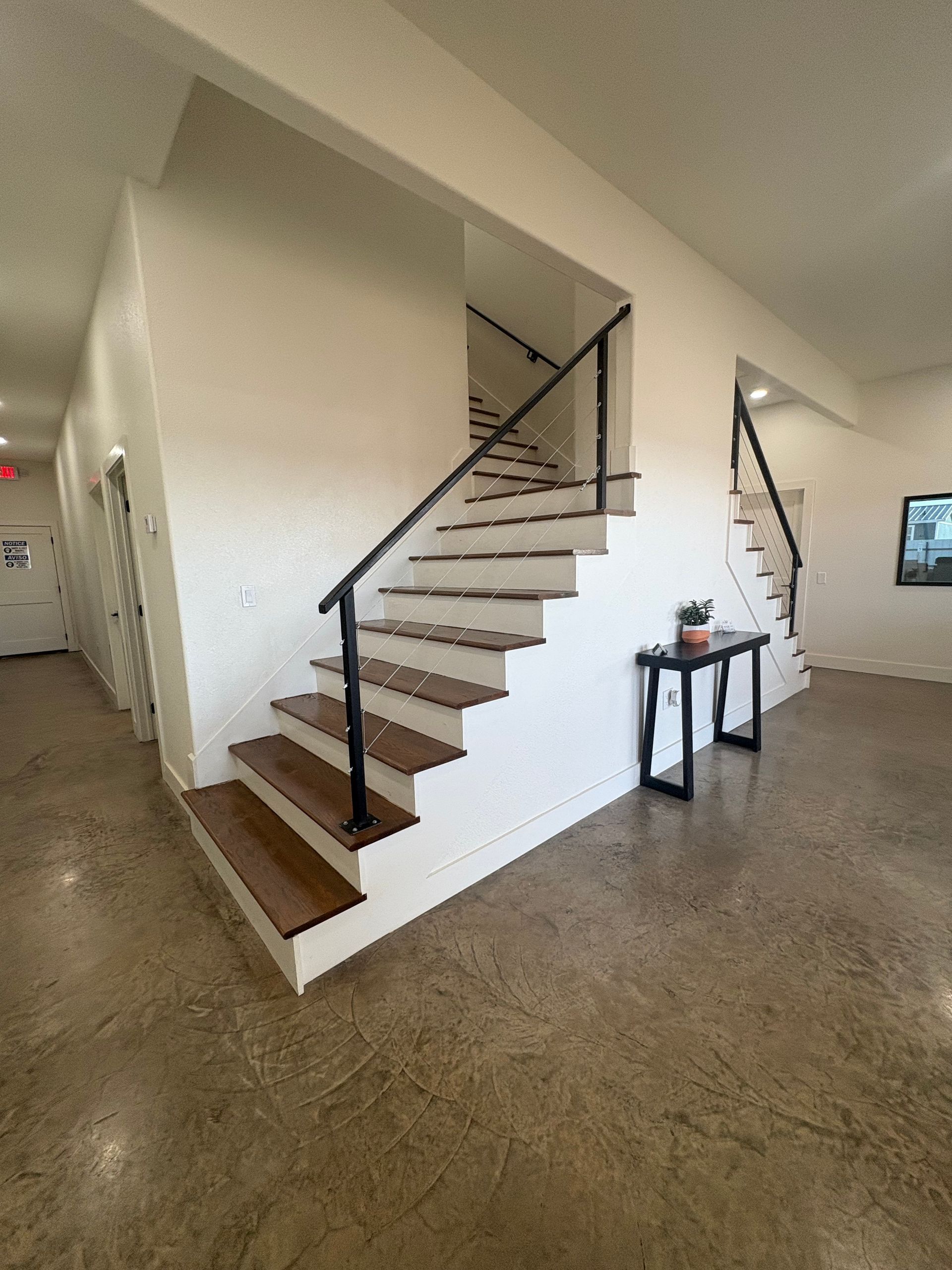 Staircase with wood steps and black railing in a building with concrete floors.