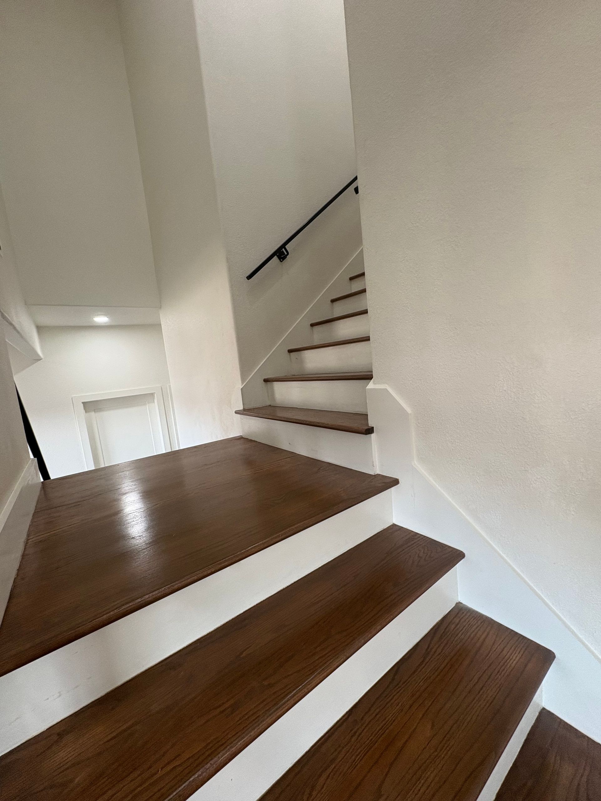 Staircase with wooden steps and white risers. A black handrail is mounted on the wall.