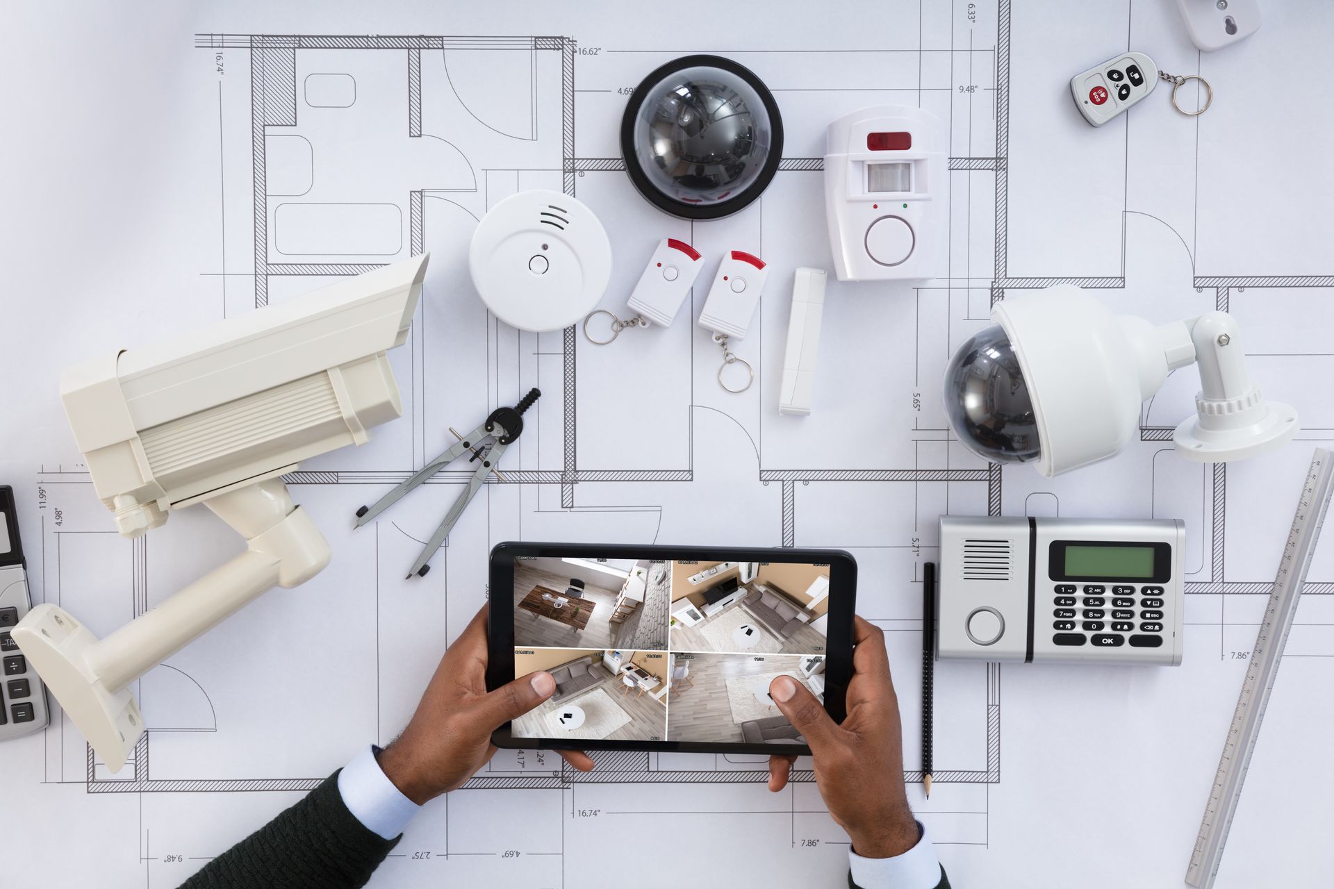 Smart home security devices on floor plan with tablet showing CCTV feeds. Smart home security devices on floor plan with tablet showing CCTV feeds.