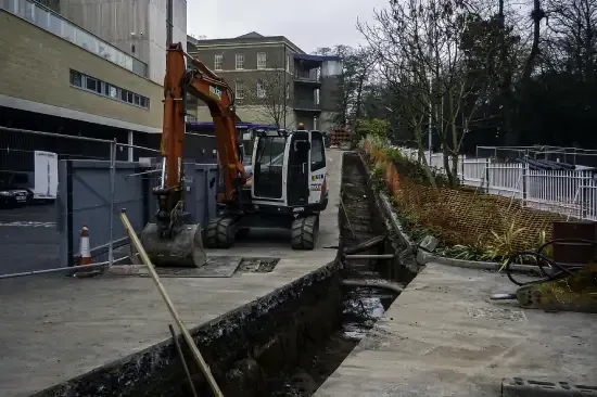 An excavator in a narrow trench beside a building, preparing construction site.