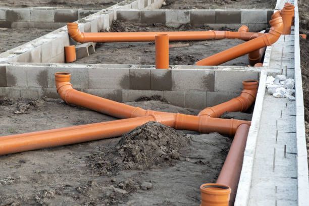 Orange PVC pipes and fittings within a concrete foundation, likely for a building's plumbing.