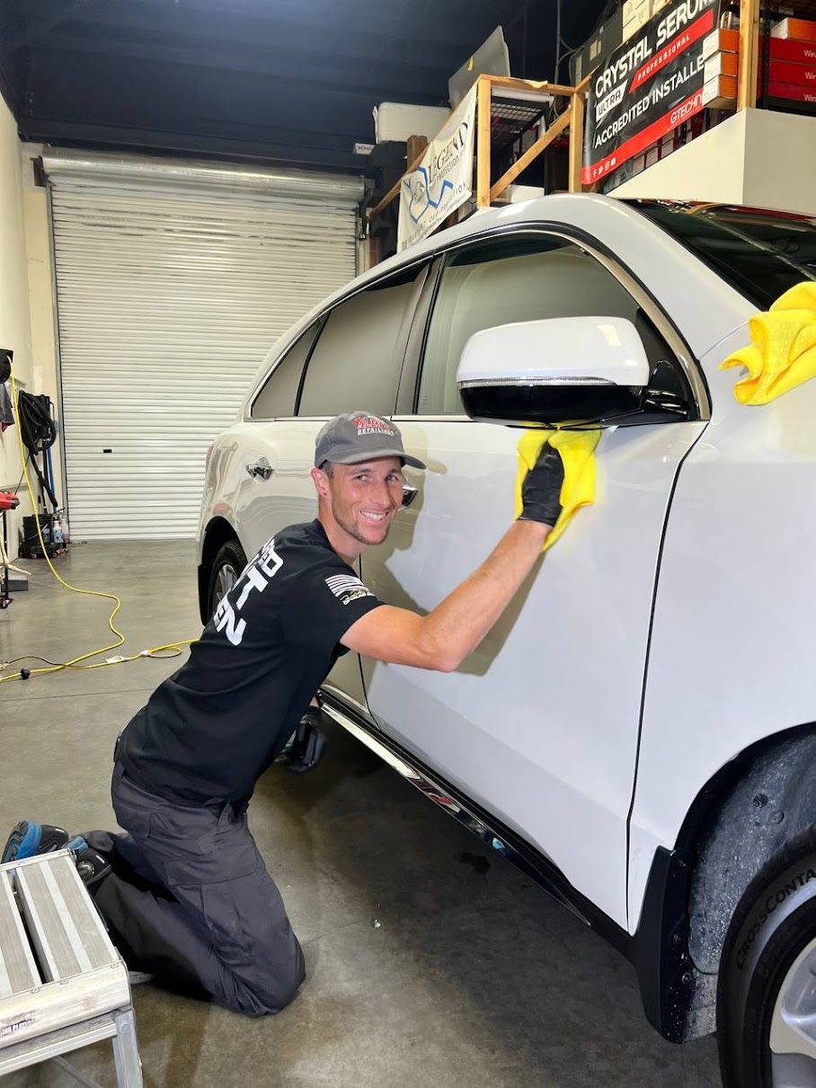 A man is kneeling down next to a white car in a garage.