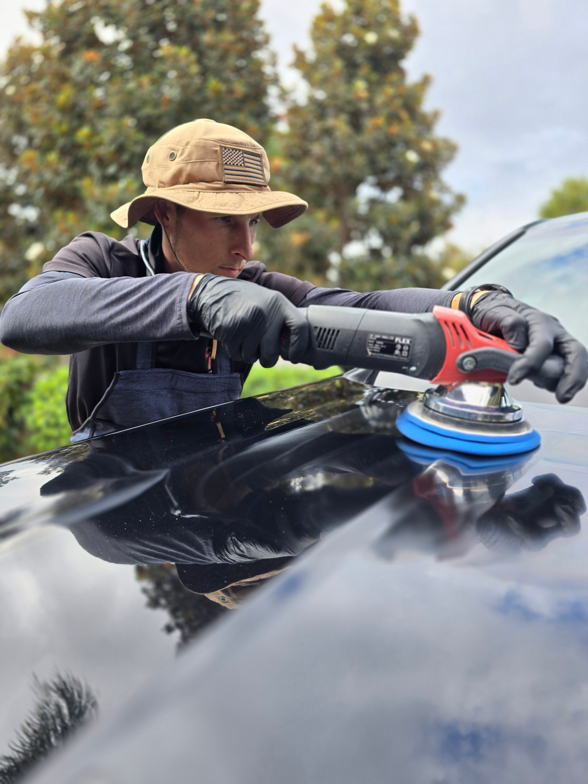 A man is polishing the hood of a black car with a machine.
