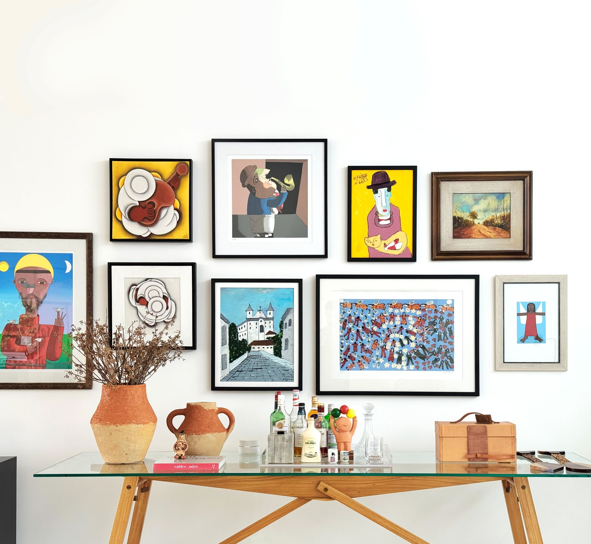 Galeria de arte emoldurada na parede acima de um aparador de vidro com objetos decorativos.