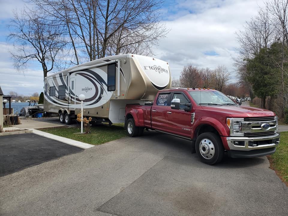 Red pickup truck towing a large fifth-wheel RV on a paved lot; blue sky.
